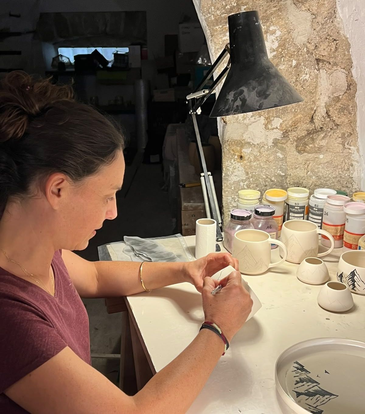 Marie Fenot peint un décor au pinceau sur une tasse, dans son atelier voûté en pierre