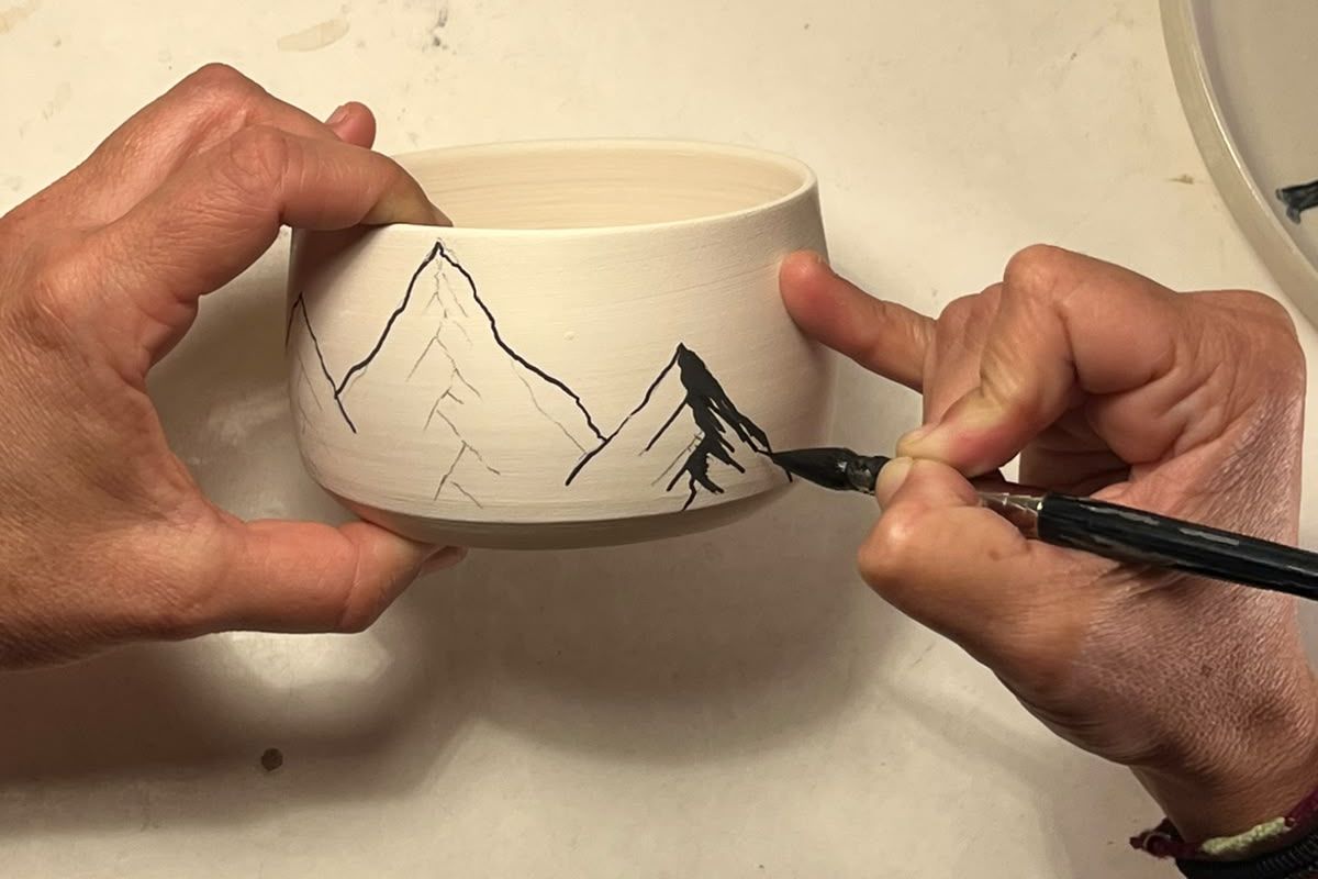 Marie peint au pinceau des montagnes à l'encre noire sur un bol en grès