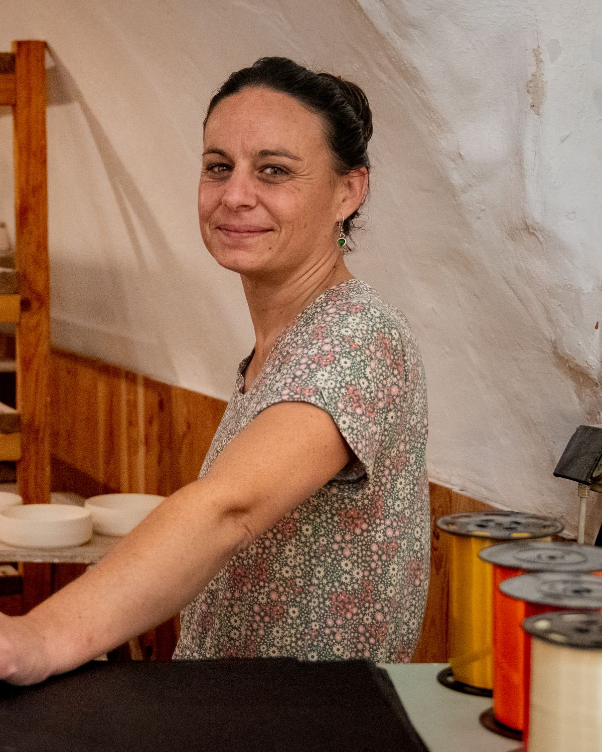 Marie Fenot souriante dans son atelier, devant les étagères de pièces en grès